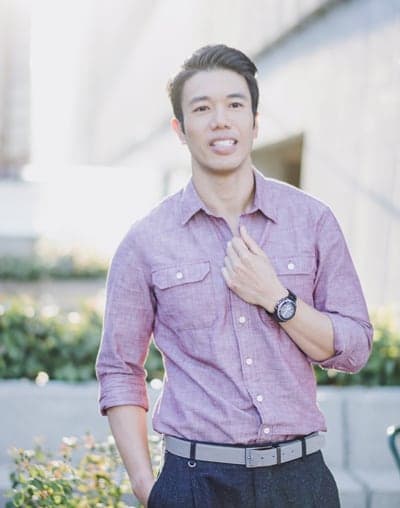 A man in purple shirt and black pants standing next to a building.